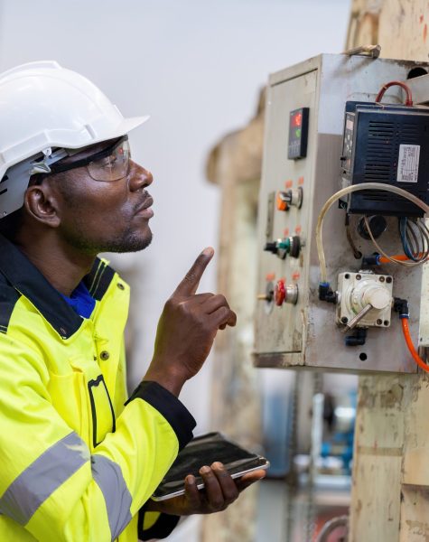 African male engineer department head Point to the electronic circuit board. of machinery in plastic and steel industries Wear a safety helmet and vest. holding laptop to work