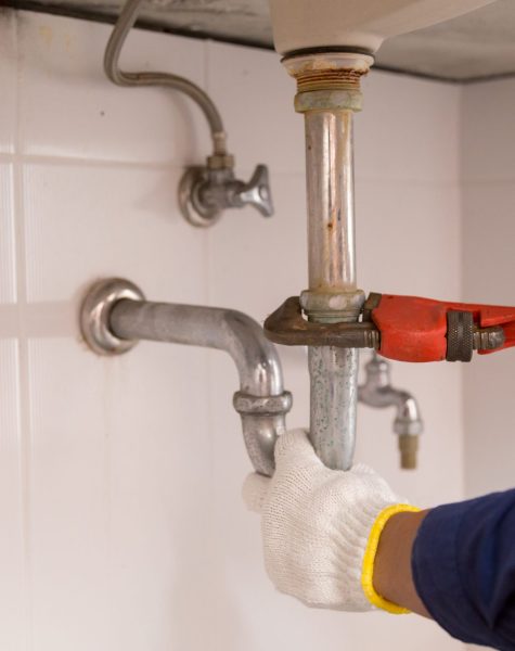 Plumber fixing white sink pipe with adjustable wrench.