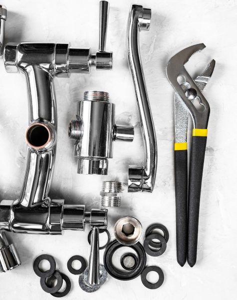 plumbing background - top view of wrench, disassembled shower faucet valve, diverter, spout, hose, various gaskets on concrete board with copyspace